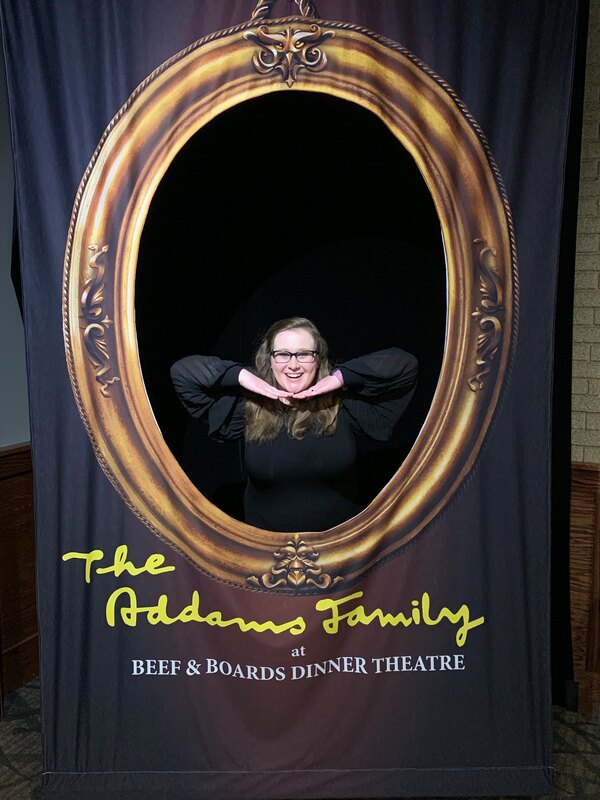 Derin is posing with her hands under her chin inside a frame. Under the frame it reads "The Addam's Family"