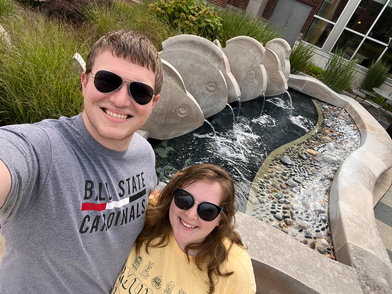 Lucas took a selfie of himself and Derin. They are both smiling in front of the Woodworth Complex fish fountain. 